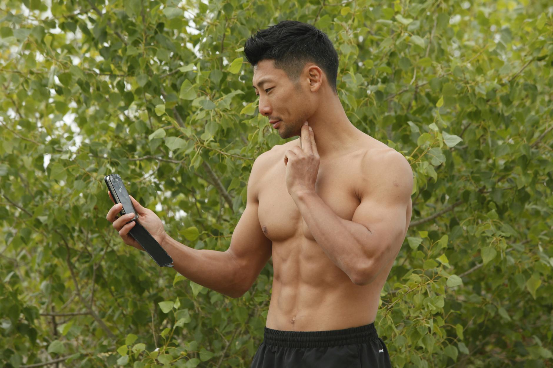 Athletic man using smartphone for pulse check in a natural setting.